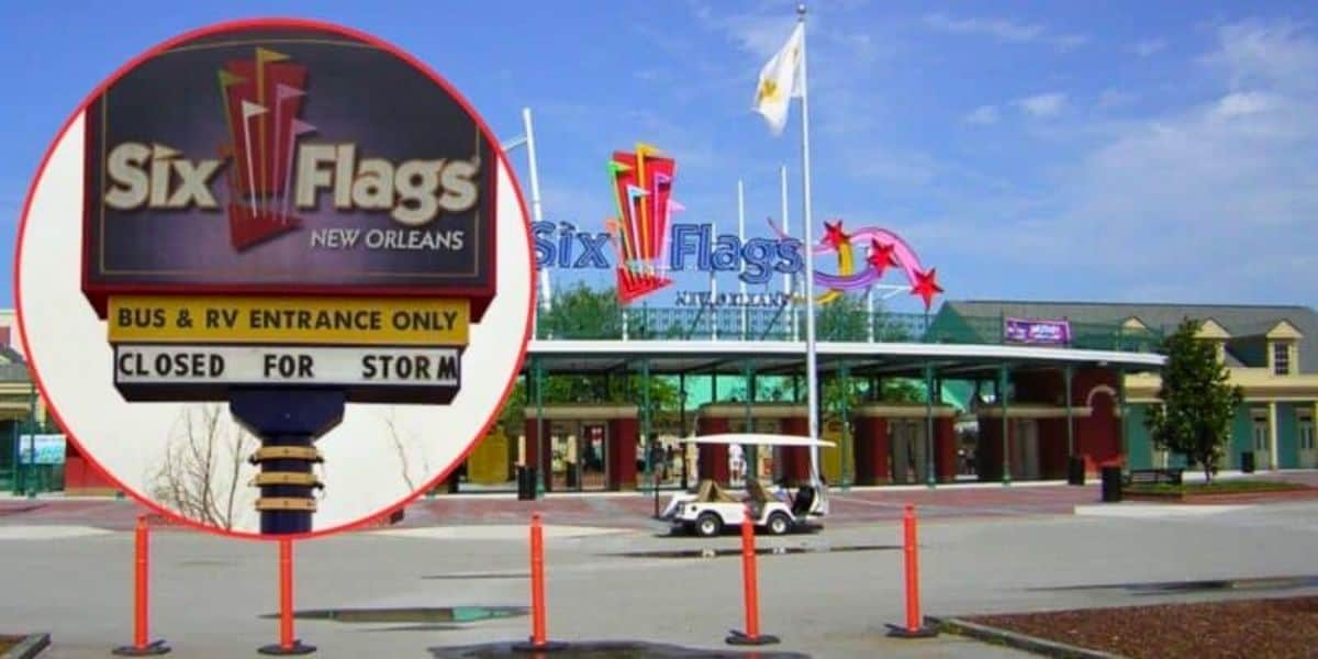 The entrance to Six Flags New Orleans shows a sign stating "Closed for Storm". The park entrance is empty with the main entrance gate and flags visible in the background, set against a blue sky. Orange safety barriers and a small vehicle are also visible.