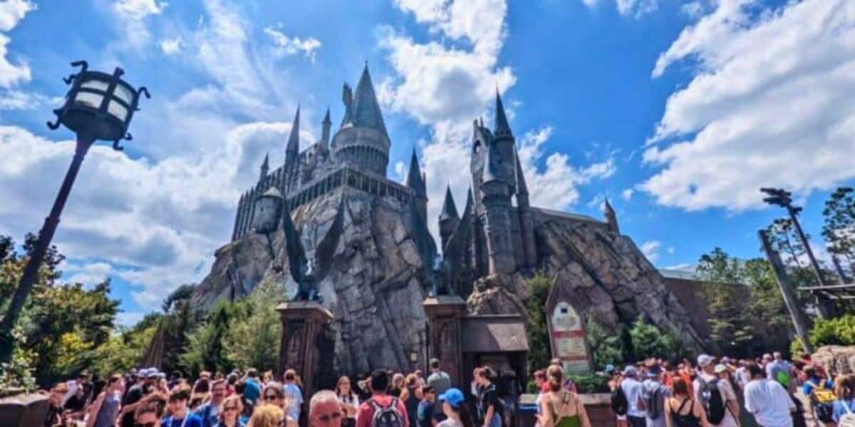 A bustling crowd of visitors under a clear sky at a theme park featuring a large, impressive castle modeled after hogwarts from the harry potter series.