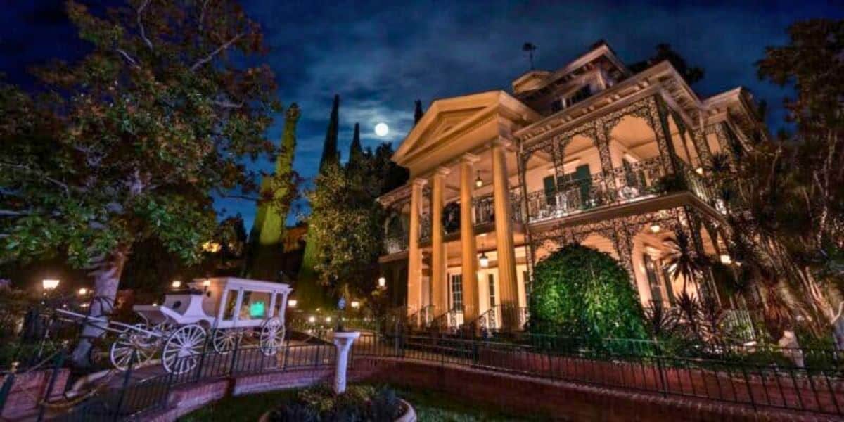 An eerie, moonlit night at a grand, haunted mansion, complete with an abandoned carriage out front.