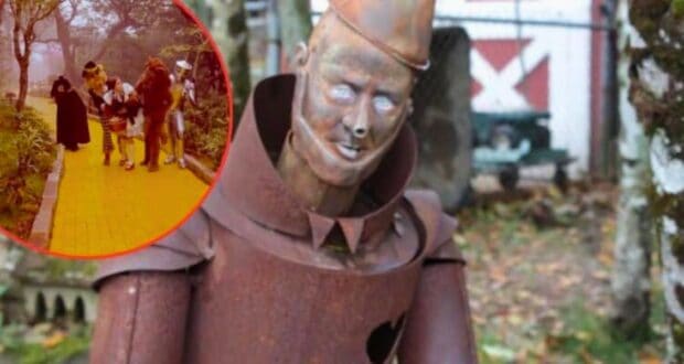 A close-up of a rusted Tin Man statue, with peeling paint and visible wear, set in an outdoor area surrounded by trees. In the top left corner, there is an inset of characters from "The Wizard of Oz" walking on the yellow brick road.