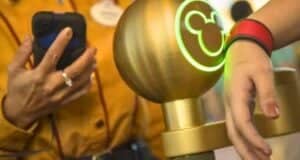 A person scans their wristband on a glowing Mickey-themed scanner, opting for the convenience of Lightning Lane access while a uniformed staff member holds a device in the background. The environment suggests an amusement park setting.