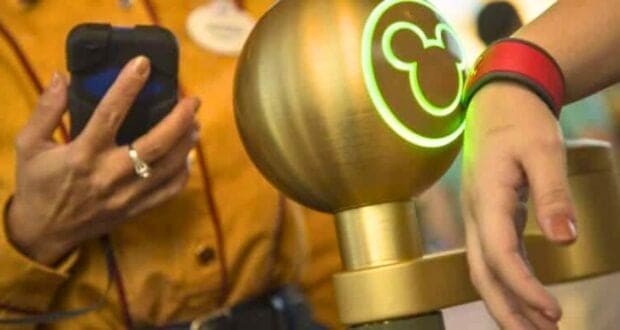 A person scans their wristband on a glowing Mickey-themed scanner, opting for the convenience of Lightning Lane access while a uniformed staff member holds a device in the background. The environment suggests an amusement park setting.