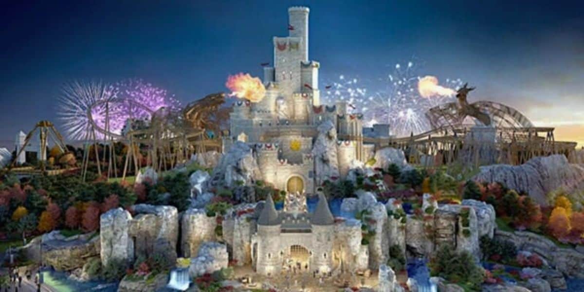 A grand castle with multiple towers stands illuminated against a twilight sky in what feels like a UK-themed Disneyland. Surrounding the castle are amusement park rides, colorful trees, and bursts of fireworks. Flamethrowers create spectacular flames, adding a magical feel to the theme park scene.
