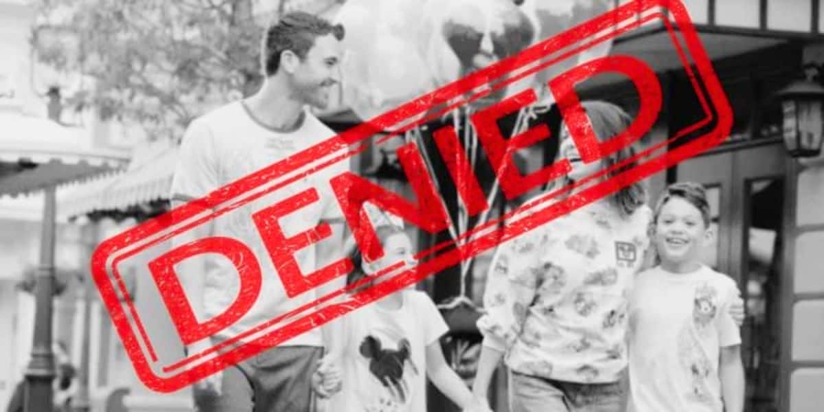 Black and white photo of a smiling family walking outdoors, reminiscent of a joyful day at Disney World. They consist of two adults and two children, holding balloons. A large red "DENIED" stamp overlays the image.
