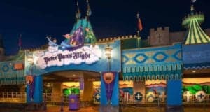 Photo of the entrance to the Peter Pan's Flight ride at a theme park. The entrance, adorned with colorful decorations featuring Peter Pan, Wendy, John, and Michael flying, is illuminated by lanterns against the dark night sky.
