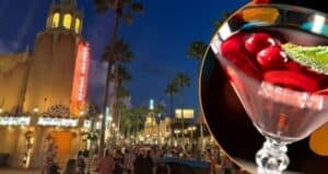 A vibrant street scene at dusk with a tower and marquee lights in the background, crowded with people. In the foreground is a close-up of a martini glass filled with a red drink, garnished with cherries and a mint leaf.