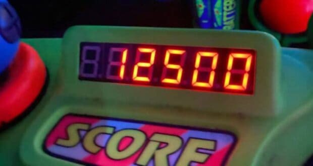 A digital score display shows "12508" in bright red numbers. The word "SCORE" is printed below the display in large, colorful letters. The surrounding area features green and blue elements from a game console.
