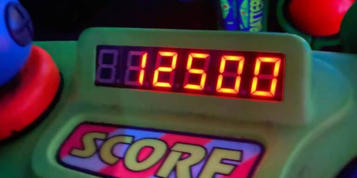 A digital score display shows "12508" in bright red numbers. The word "SCORE" is printed below the display in large, colorful letters. The surrounding area features green and blue elements from a game console.