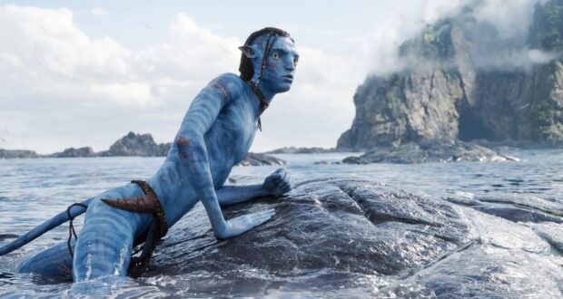 A blue-skinned, humanoid figure resembling an avatar with pointed ears and braided hair is perched on a rock in the ocean.