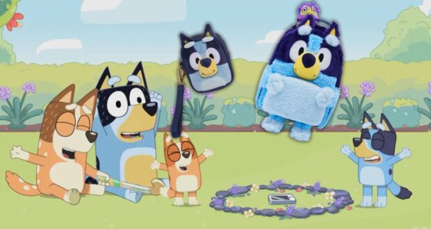 A cartoon family of dogs sits on grass with arms raised, surrounded by flowers and a toy circle. A keychain, lunch bag, and plush backpack, all resembling a blue dog with a unicorn hat, are scattered over the scene.