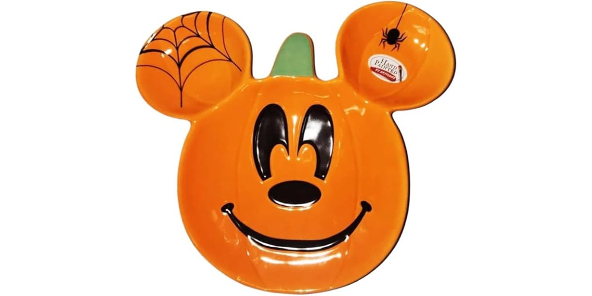 An orange pumpkin-shaped plate with features resembling a cartoon character's face, including large eyes and a smiling mouth. One ear features a spiderweb design with a small black spider.