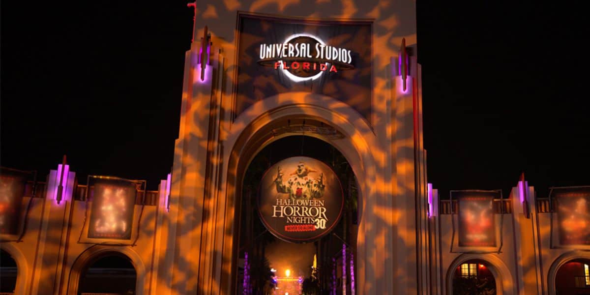 Illuminated entrance of Universal Studios Florida decorated for Halloween Horror Nights 30. The archway displays spooky light patterns and a large circular sign with event details. It is nighttime, enhancing the eerie atmosphere.