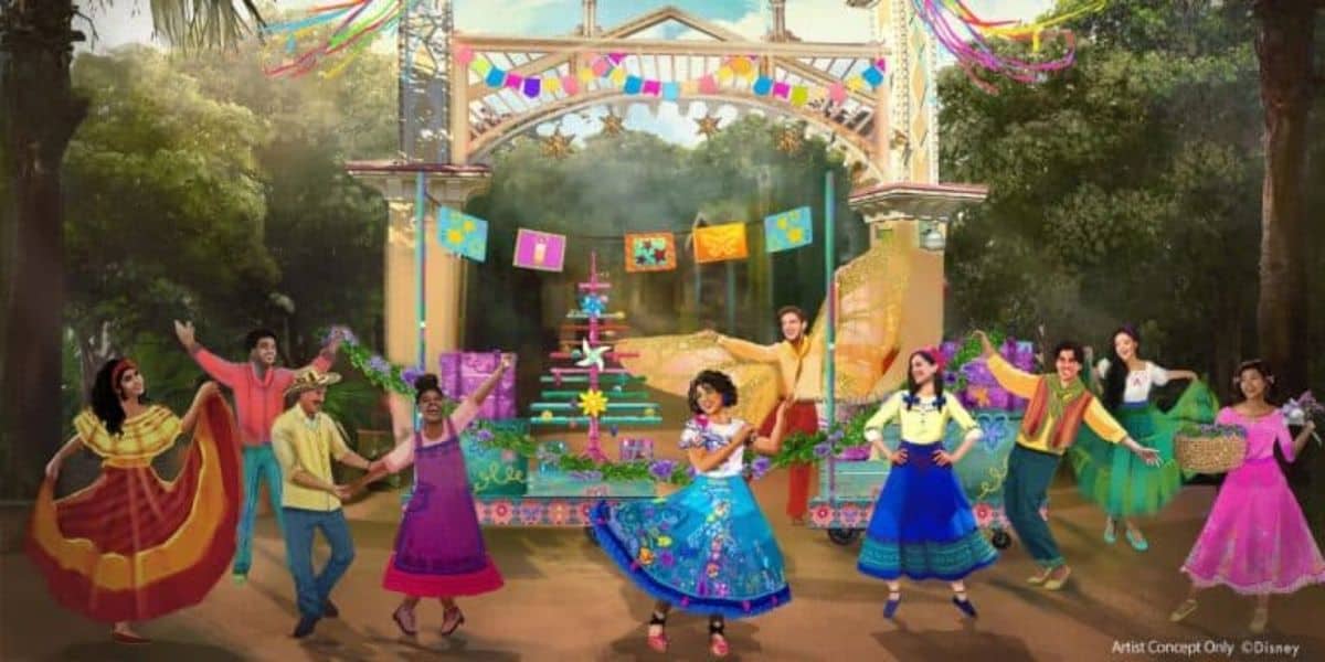 Colorful festival scene with dancers in vibrant traditional costumes performing in front of a decorated stage. Banners, flags, and greenery surround the area, creating a festive atmosphere. People hold baskets and flags, adding to the lively celebration.