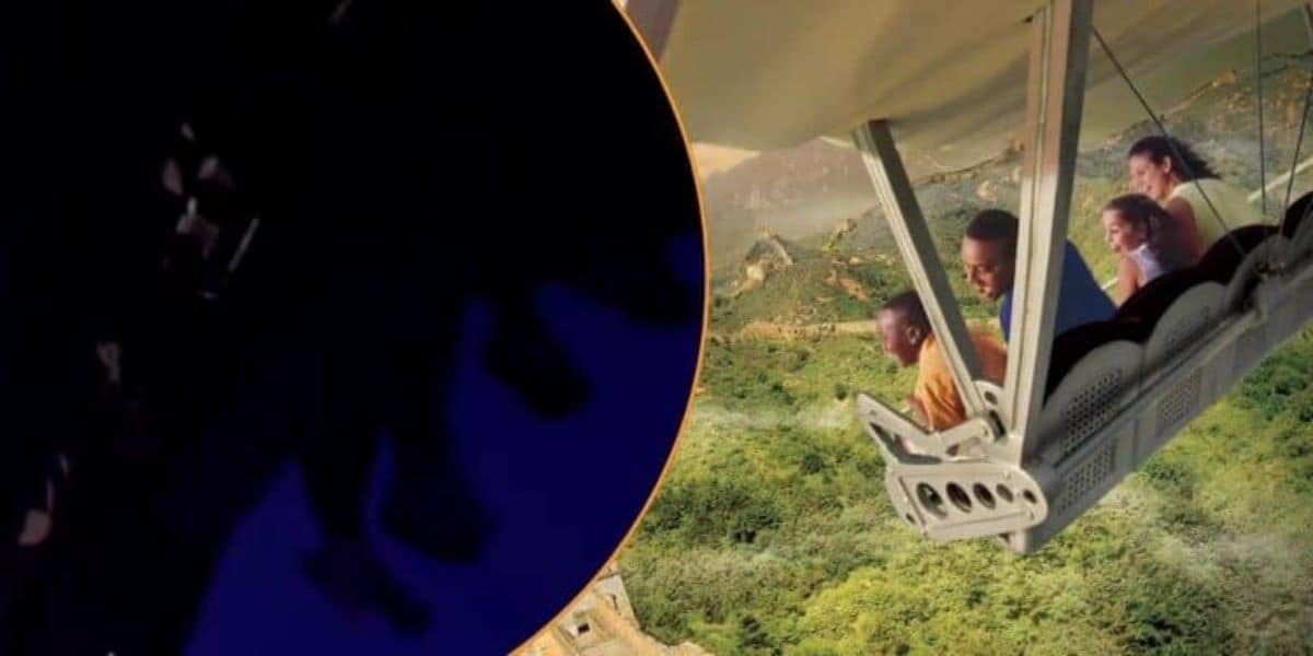 People are on a ride, simulating a flight over a green landscape. They're seated in what appears to be an amusement park ride, with a partially darkened foreground. The image gives a sense of excitement and adventure.