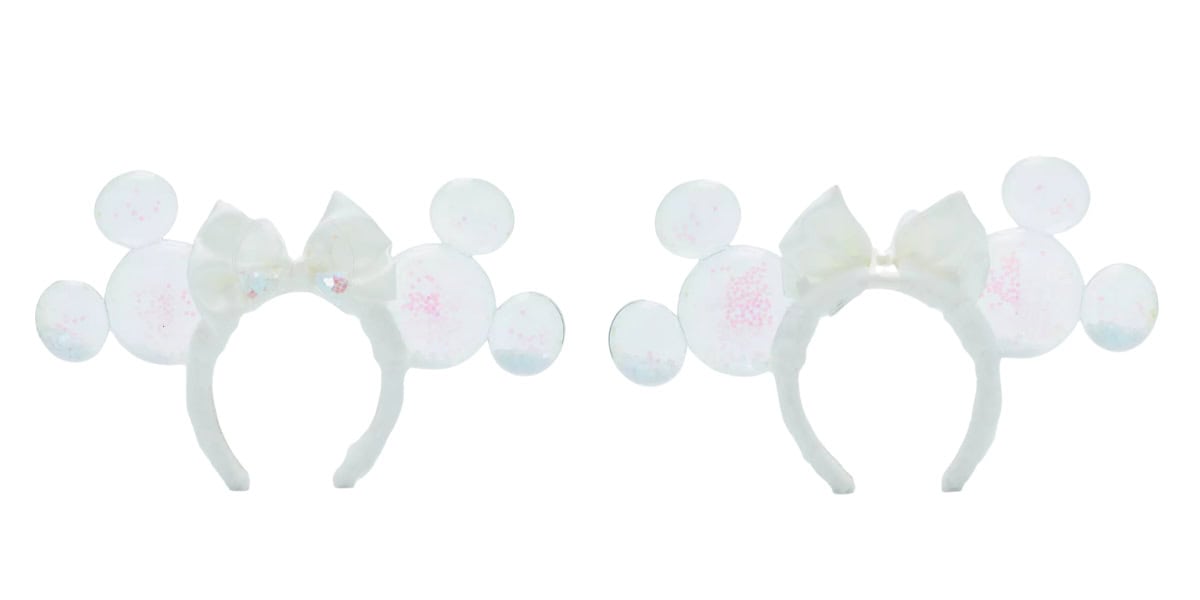 Two white headbands with large, round Mickey Mouse ears. Each headband has a glittery, translucent bow in the center. The headbands are set against a plain white background.