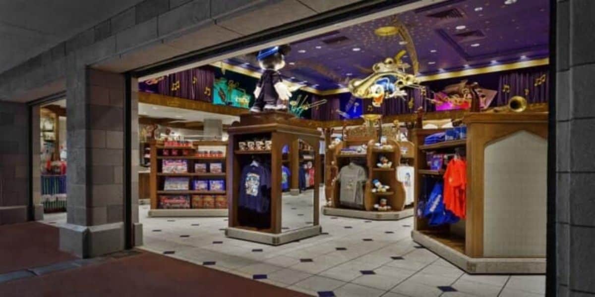 The image shows a brightly lit retail store with various themed merchandise. Shelves and racks display clothing, plush toys, and other items. The decor features magical motifs, including a prominent golden wand and musical notes on the walls and ceiling.