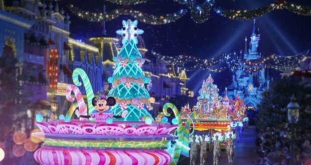 A festive parade at night features brightly lit floats with colorful decorations, including a Christmas tree and candy motifs. A character with large ears and a polka dot bow is on a float. String lights adorn the buildings in the background.