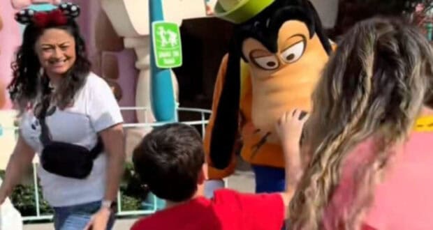 A boy grabs A Disney character performer dressed as Goofy's nose.