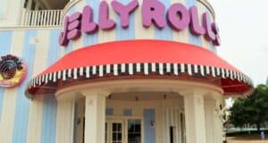 A colorful building features a sign with large purple letters spelling "Jellyrolls" above a red and white striped awning. The facade is blue and white striped, and there's a multicolored logo on the side wall.