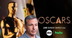 A man stands in front of an Oscars backdrop featuring a golden statuette and event details. The text reads "Oscars Live Sunday March 2nd" with ABC and Hulu logos.