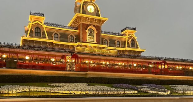 The image shows the entrance to Magic Kingdom Park at Walt Disney World Resort in rainy, cold weather.