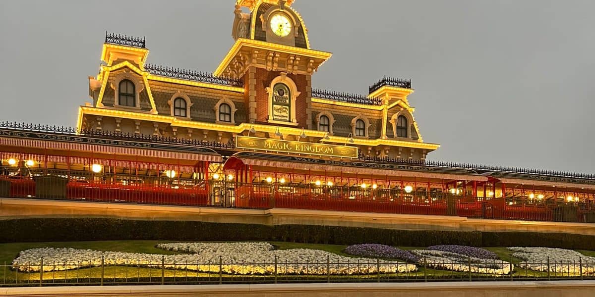 The image shows the entrance to Magic Kingdom Park at Walt Disney World Resort in rainy, cold weather.