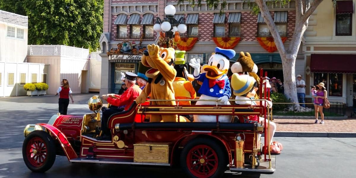 Donald Duck, Pluto, and other characters wave from a vintage red fire truck on Disneyland Park's Main Street, U.S.A.