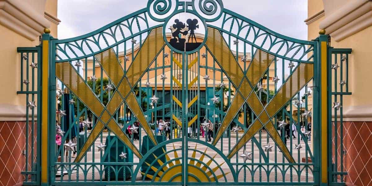 Ornate green and gold gate with star decorations at an amusement park entrance. People are visible in the background near the check-in area. The sky is overcast, creating a soft, diffused light.