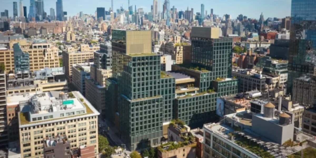 Aerial view of a cityscape featuring modern high-rise buildings with green terraces. The background displays a sprawling urban skyline with numerous skyscrapers under a clear blue sky.