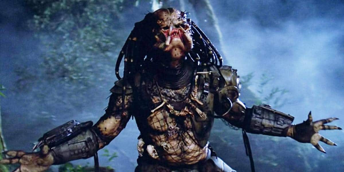 A menacing alien creature with dreadlock-like hair, armored gear, and reptilian skin stands in a misty forest, mouth open in a roar and arms spread wide.