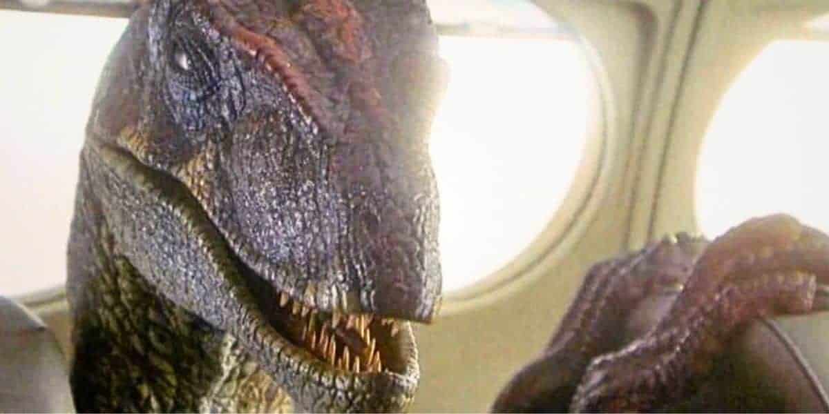 A close-up of a dinosaur with sharp teeth sitting inside an airplane, next to a window, under bright light.