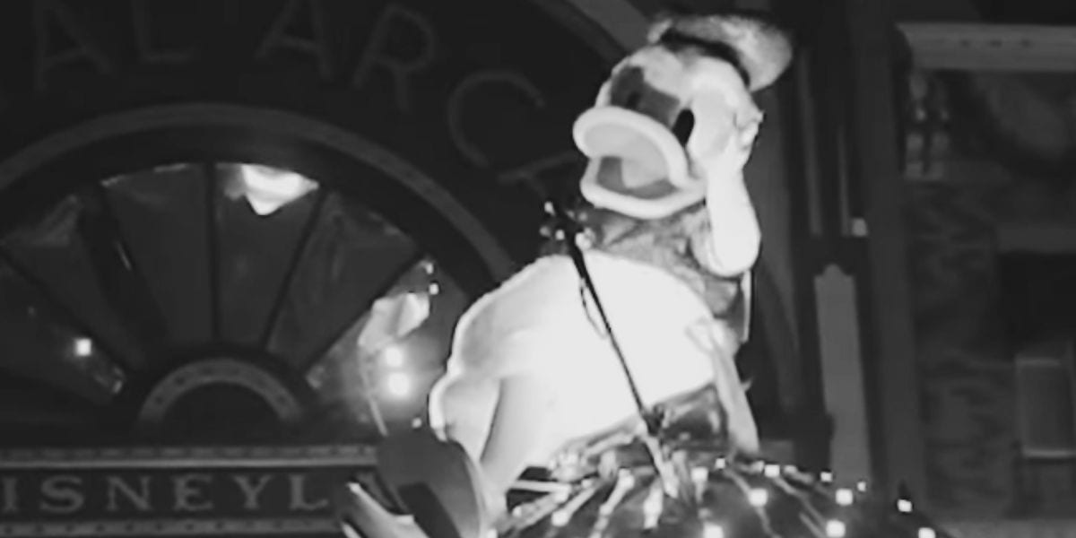 Black and white photo of a Donald Duck costume character on a Disney parade float decorated with lights.