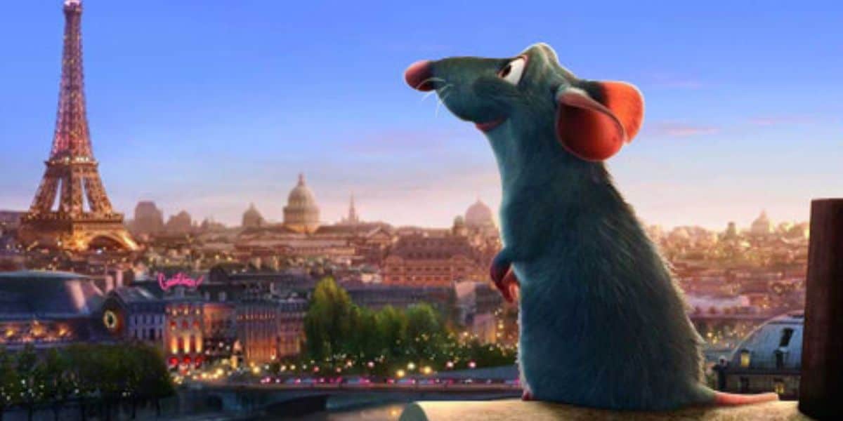 A blue rat with large pink ears sits on a rooftop, gazing at the Paris skyline with the Eiffel Tower in the background at sunset.