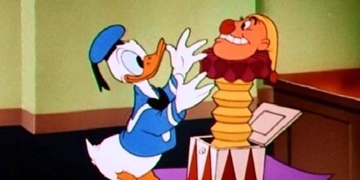 Donald Duck, dressed in his usual blue sailor outfit, looks surprised as he opens a jack-in-the-box with a clown popping out. The scene appears to be indoors with a green and brown background.