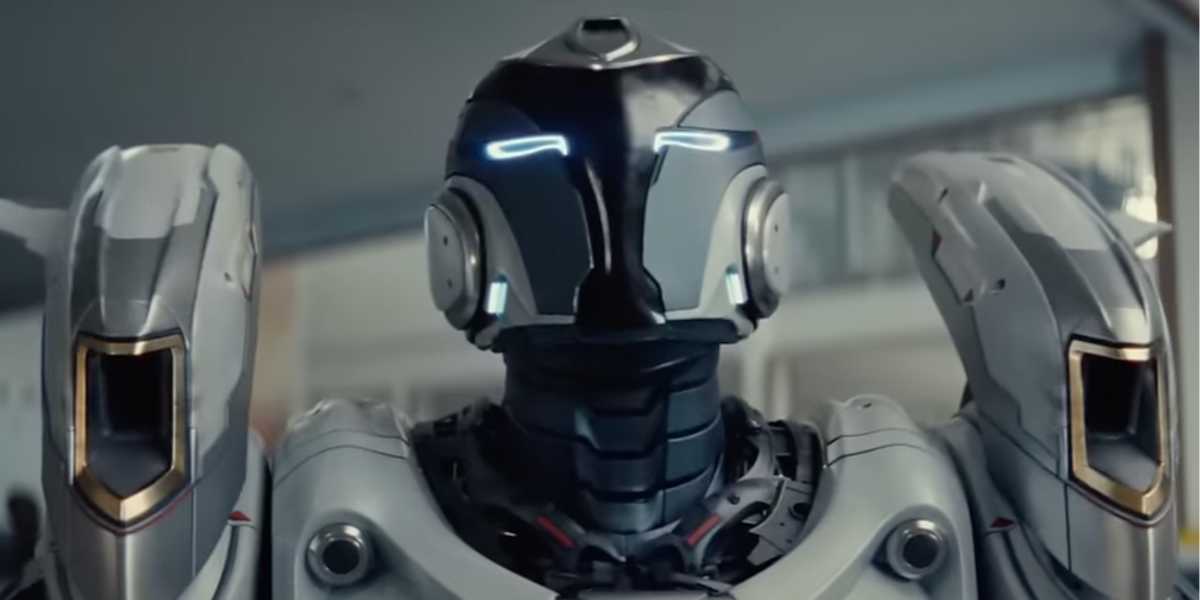 A futuristic humanoid robot with a sleek, metallic body and glowing blue lights on its face stands upright indoors, looking directly ahead.