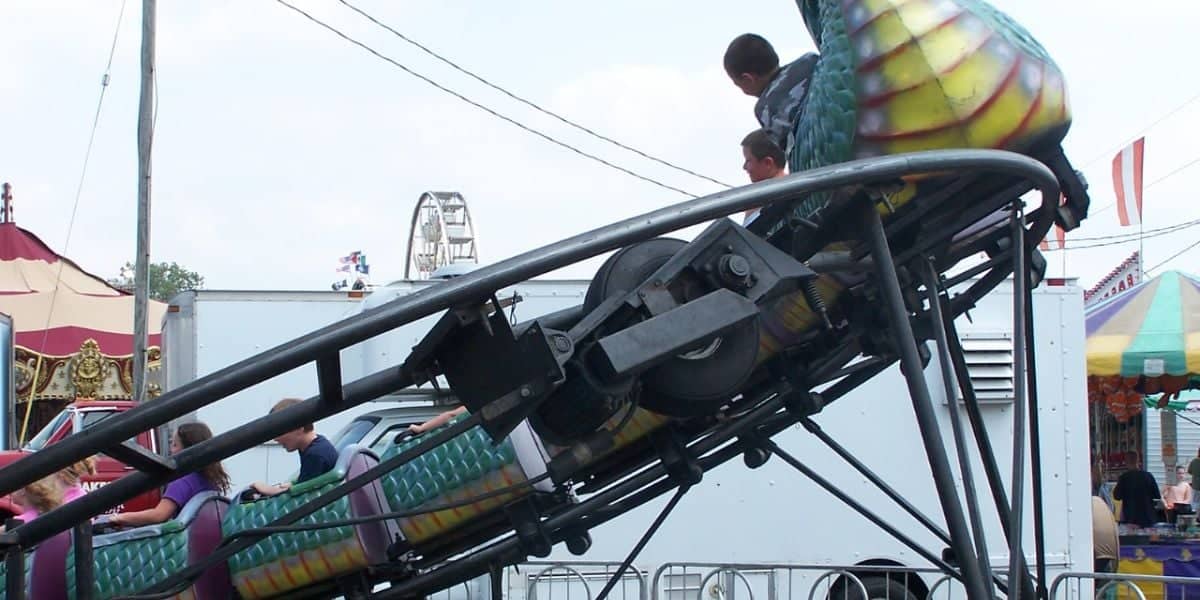 Children ride a small dragon-shaped rollercoaster at an outdoor fair.