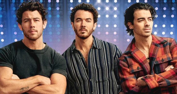 Three men with short, curly dark hair stand side by side against a backdrop of blue and purple lights. The men wear casual shirts and have neutral expressions, looking slightly off-camera.
