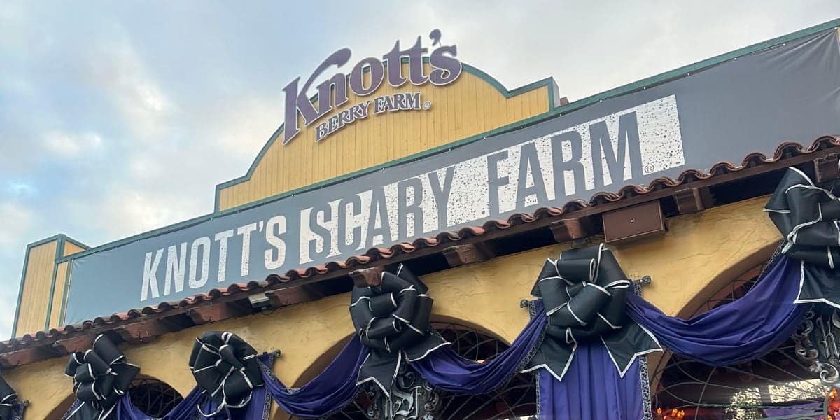 The entrance to Knott's Berry Farm is decorated for Halloween with a large sign that reads "Knott's Scary Farm," black bows, and purple drapes.