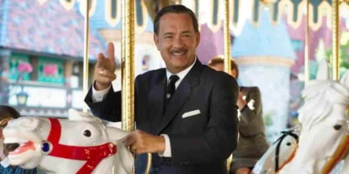 A man in a suit smiles and waves while riding a white carousel horse. The background features colorful decorations.