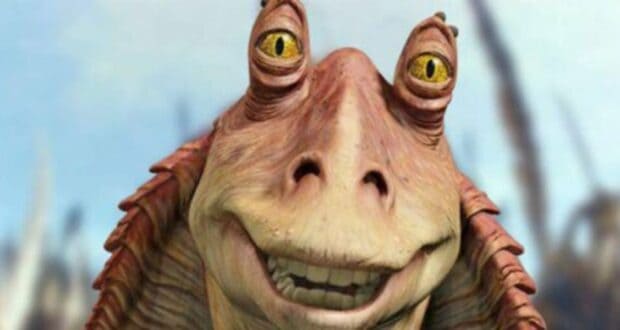 A close-up of Jar Jar Binks, a fictional alien character with yellow eyes and a wide smile, from the Star Wars movie series, against a blurred outdoor background.