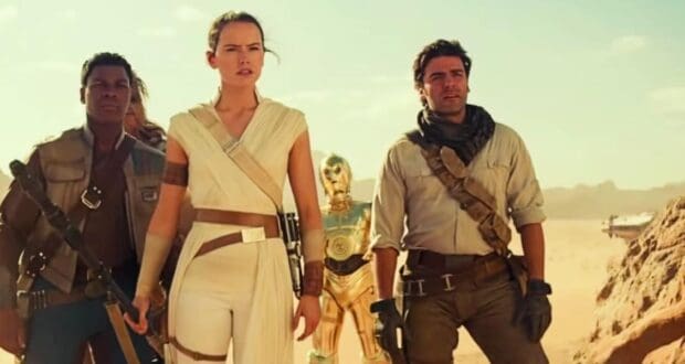 Three people dressed in sci-fi adventure clothing stand confidently in a desert, with a gold humanoid robot and spaceship in the background under a bright sky.