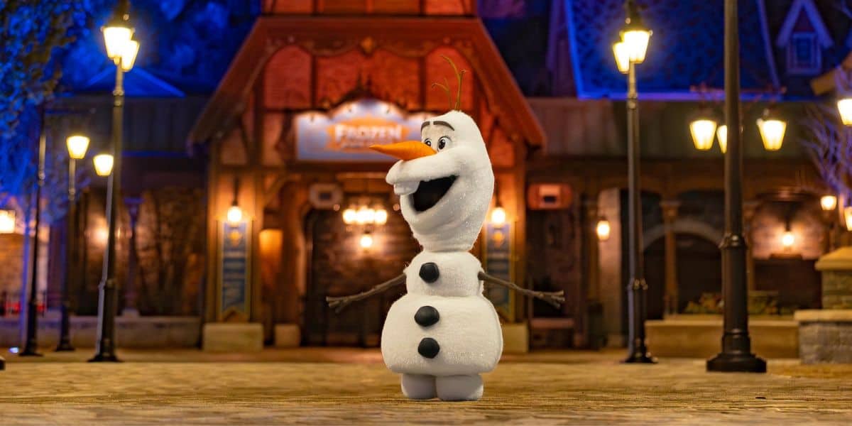 Olaf greets guests with open arms outside a glowing nighttime venue, spreading Frozen magic to everyone at the park.