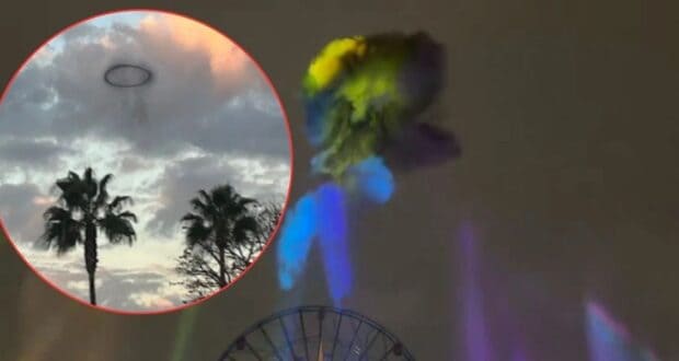 A dark ring-shaped cloud floating above palm trees and a ferris wheel in a cloudy sky, with colorful lights beaming upward.