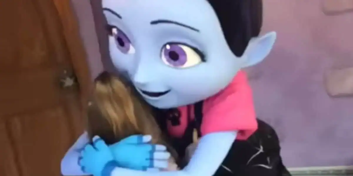 A beloved blue Disney character warmly embraces a young guest near a park entrance, capturing the magic of a character meet-and-greet.