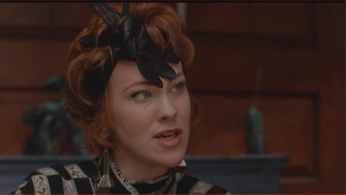 Catherine O'Hara, with signature red hair and a black feathered hat, delivers an emotional scene inside the Haunted Mansion.