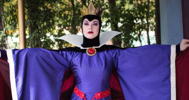 The Evil Queen from Snow White greets guests in her jeweled crown, dramatically displaying her flowing purple robe.