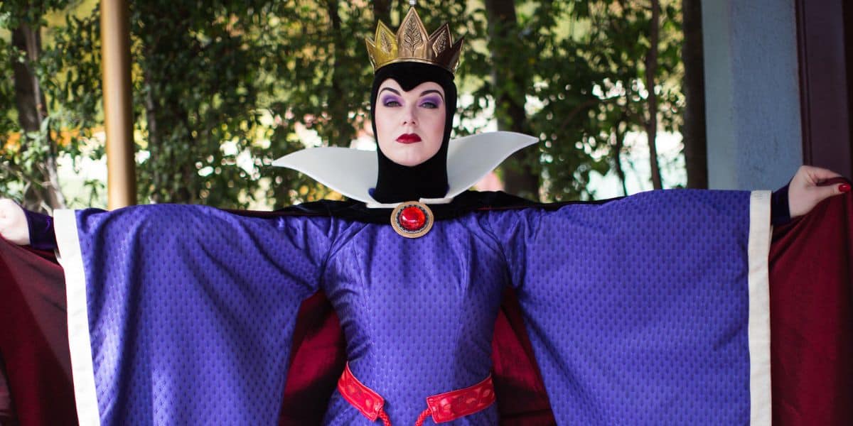 The Evil Queen from Snow White greets guests in her jeweled crown, dramatically displaying her flowing purple robe.