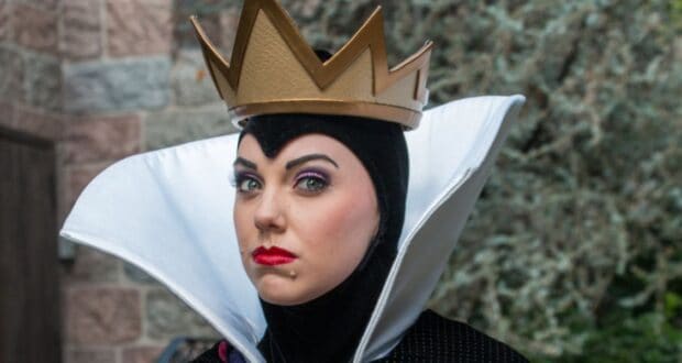 The Evil Queen in her iconic gold crown and dramatic high white collar greets visitors outdoors at the theme park.