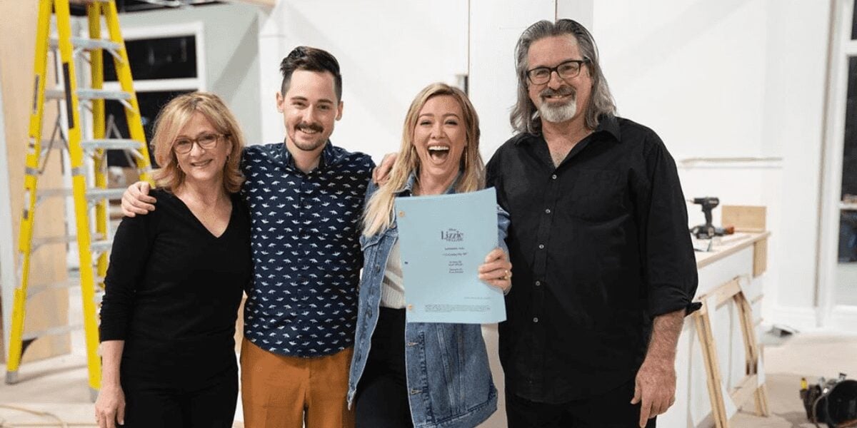 Cast members in a Disney Parks backstage area smile together, one holding a script, embodying friendly teamwork and behind-the-scenes magic.