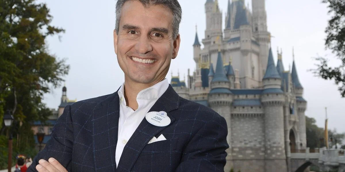 Sharp-dressed guest beams in front of a storybook castle at Disneyland, ready for a magical day of adventure and fun.